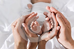 cropped view of parents holding in their hands little baby feet, happy