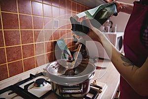 Cropped view of pastry chef or chocolate maker throwing chocolate tablets into water bath to heat and cook melted chocolate mass