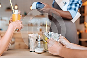 cropped view of people paying with cash, waiter standing behind