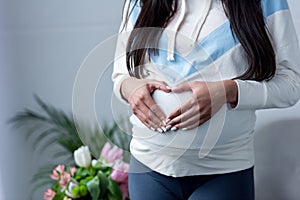 cropped view of pregnant girl making heart symbol with hands on her belly