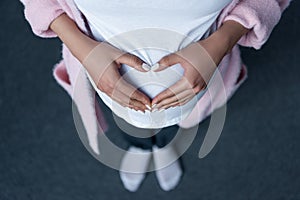 cropped view of pregnant girl making heart symbol with hands on her belly