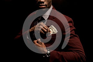 cropped view of rich african american man putting dollar banknotes into pocket