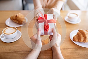 Cropped view of romantic lady and her boyfriend with gift at coffee shop, celebrating Valentine`s Day