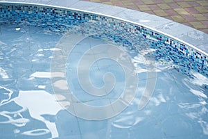 Cropped view of a round outdoor swimming pool with blue mosaic ceramic tiles, with blue water. Background with copy