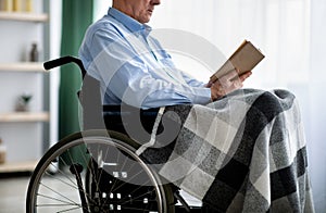 Cropped view of senior disabled man in wheelchair reading book indoors