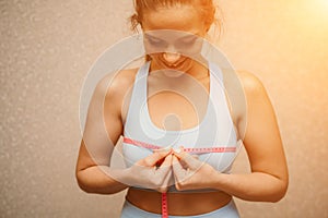 Cropped view of slim woman measuring breasts with tape measure at home, close up. A European woman checks the result of