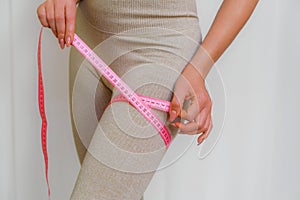 Cropped view of slim woman measuring her leg with tape measure at home, close-up. An unrecognizable European woman