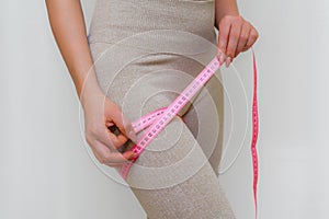 Cropped view of slim woman measuring her leg with tape measure at home, close-up. An unrecognizable European woman