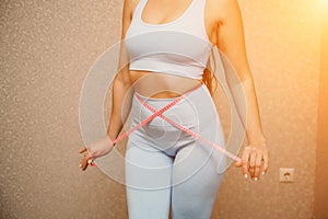 Cropped view of slim woman measuring waist with tape measure at home, close up. Unrecognizable european woman checking