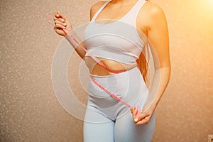 Cropped view of slim woman measuring waist with tape measure at home, close up. Unrecognizable european woman checking