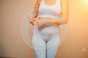 Cropped view of slim woman measuring waist with tape measure at home, close up. Unrecognizable european woman checking