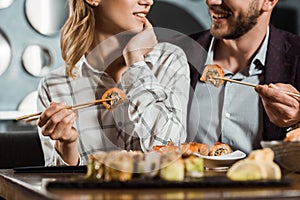 Cropped view of smiling happy couple eating sushi