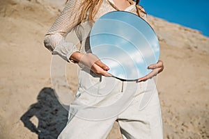 cropped view of stylish girl holding mirror with reflection of blue sky