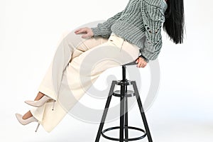 Cropped view of stylish woman in white trousers sits on a wooden black chair on white background