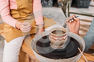 cropped view of teacher and kid painting ceramic pot on pottery wheel