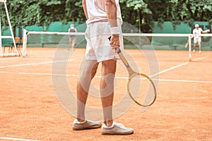 cropped view of tennis player holding retro wooden racket and standing on tennis