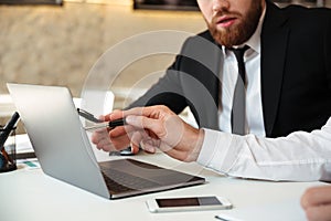 Cropped view of two business partners discussing new project while working with laptop in office