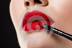 cropped view of woman applying red lipstick with cosmetic brush