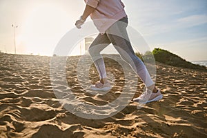 Cropped view of woman burning calories while running on the sandy beach at sunset. People, active and healthy lifestyle