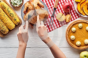 Cropped view of woman cutting roasted turkey near pumpkin pie and grilled vegetables served on white wooden table with