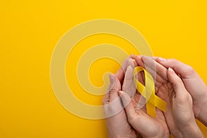 Cropped view of woman and man holding yellow ribbon on colorful background, international childhood cancer day concept.