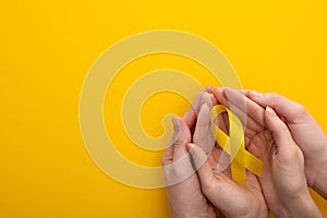 Cropped view of woman and man holding yellow ribbon on colorful background, international childhood cancer day concept. photo