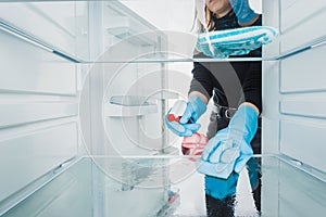 Cropped view of woman in rubber gloves cleaning refrigerator with detergent