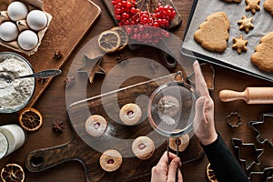 Cropped view of woman sieving sugar powder on Christmas cookies at wooden table.