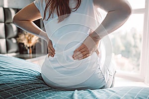 cropped view of woman suffering from backache after her wake up sitting on bed. Healthcare and medicine