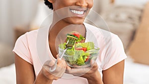 Cropped view of young black lady eating fresh vegetable salad indoors, panorama