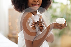 Cropped view of young black woman applying cream on her body, pampering her skin after shower at home, closeup