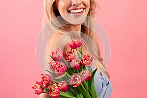 Cropped view of young lady with bouquet of lovely tulips on pink studio background, closeup