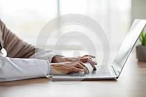 Cropped of woman doctor typing on laptop keyboard