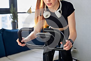 cropped woman working out at home on the exercise bike, young female cycling for good health.