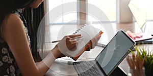 Cropped of young entrepreneur woman taking notes while sitting in front her computer tablet with keyboard case.