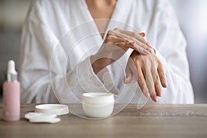 Cropped of young lady massaging hands, using cream