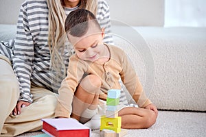 cropped young mother and child playing game with toys at home together, on floor.