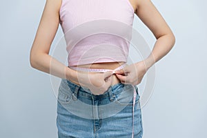 Cropped young woman in white clothes show loose pants after weightloss hold measure tape on waist