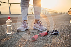 Croppped image of athlete legs wearing pink sneakers and standing on an asphalt treadmill next to a lying down jumping rope and