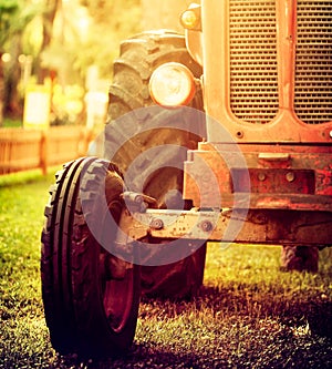 Old vintage red tractor standing on a farm field at sunset.