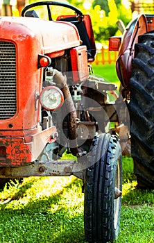 Old vintage red tractor standing on a farm field at sunset.