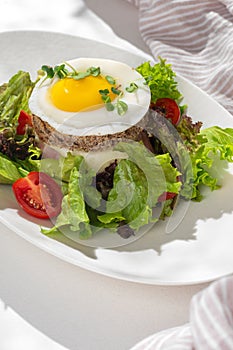 Croque madam sandwich with cheese, ham and egg on a plate on a light table. Hearty homemade breakfast.