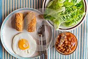 Croquettes, fried egg, fresh vegetables, white kidney beans in t