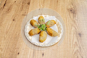 Croquettes stuffed with bÃ©chamel and chicken garnished with sprouts on recycled cardboard plate