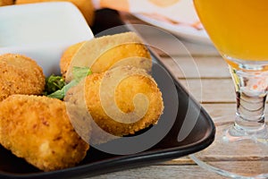 Croquettes or traditional Spanish homemade croquettes on a black plate with a beer on the side. Tapas food concept photo