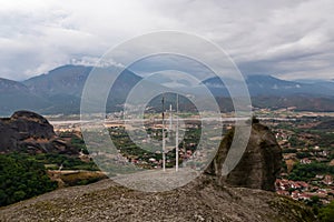 Meteora - Cross with bell on top of rock Aghio Pnevma (Holy Spirit). Panoramic view on valley between village of Kastraki