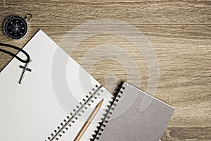 A cross on book with compass and grey notebook over the wooden table.