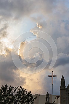 Cross on building with towers and trees against large colorful clouds