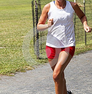 Cross country female racing in white top and red shorts on gravel path
