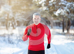Cross country running in winter. Happy fit senior man jogging in snowy forest on sunny morning